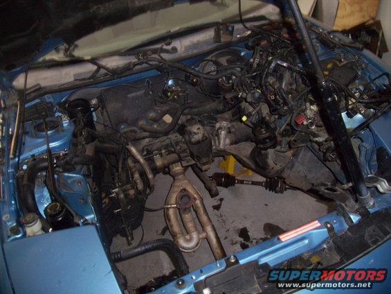 Blue car engine bay with engine removed, showing wiring and exhaust components