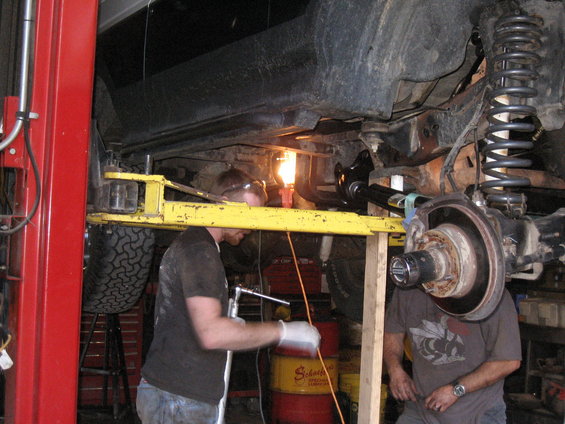 Mechanics working on the undercarriage of a vehicle on a lift, with a focus on the suspension and brake components