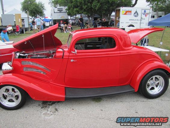 Red coupe hot rod with hood and trunk open, chrome wheels, custom side vents