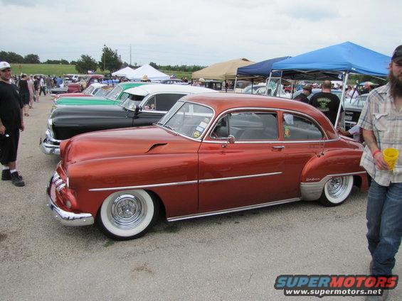 Customized orange classic sedan with whitewall tires parked in a row at a car show