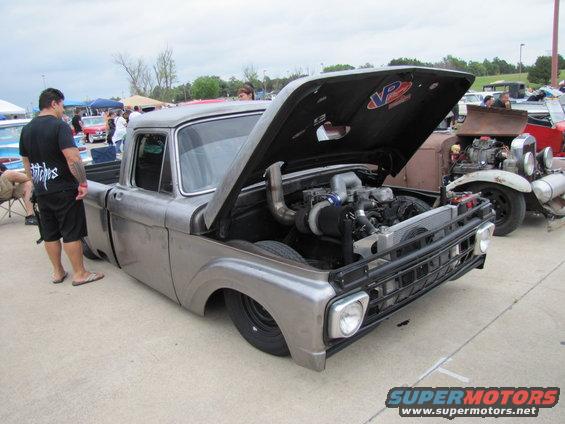 Pickup truck with hood open showing a turbo engine. Another vintage car is parked behind it