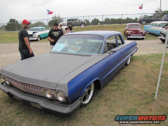 Blue and gray 1963 Impala with custom wheels, parked outside. Other cars and people around