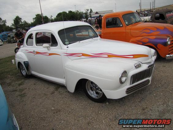White hot rod with red and yellow flame decals on the side, chrome wheels, and a lowered stance