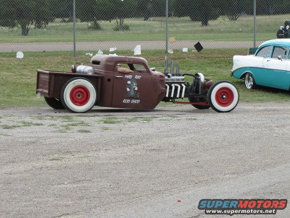 Brown rat rod pickup truck with red wheels and white walls, "Mad Rat Rod Shop" text