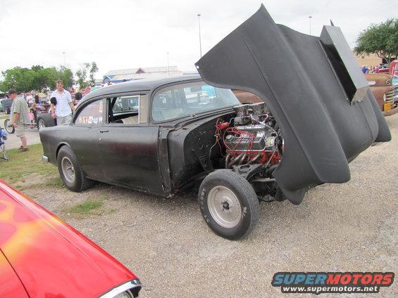 Black 1955 Chevrolet hot rod with hood open, showing V8 engine and headers. Modified body, drag racing tires