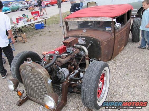 Rusty hot rod with red roof, exposed engine, and whitewall tires