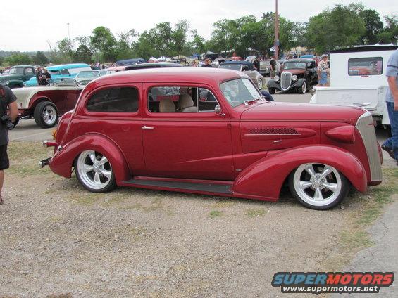 Red hot rod sedan with custom wheels parked at an outdoor car show