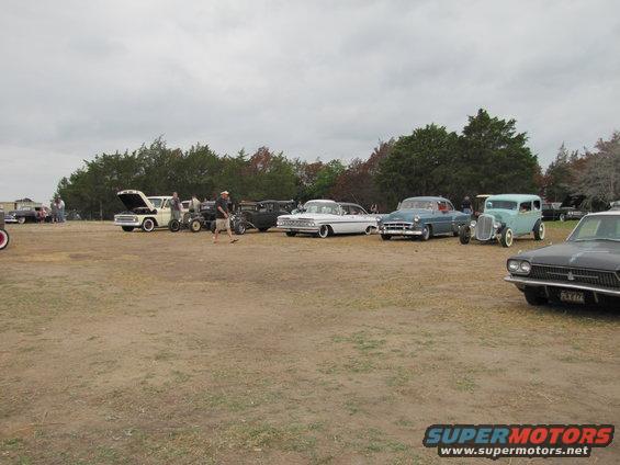 Outdoor car show with several classic cars and people gathered