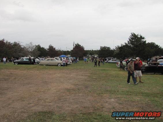 People milling around a field with many classic cars parked