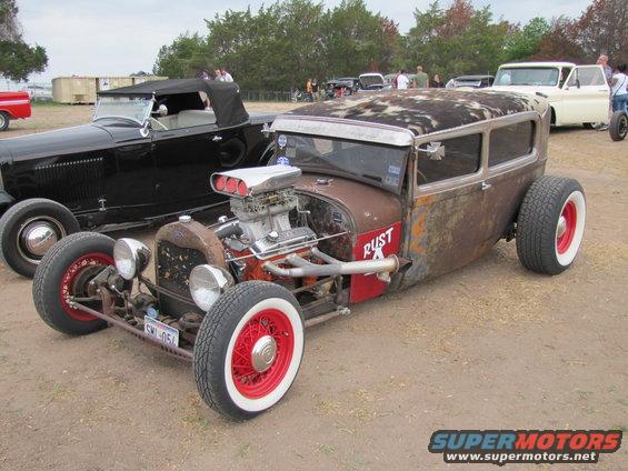 Rusty hot rod sedan with a supercharger, red wire wheels, and white wall tires