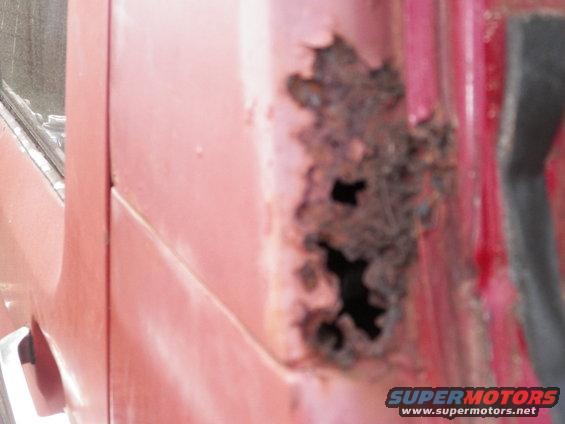 Close-up of severe rust damage with holes on a red vehicle's door panel