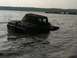 1990 Ford Bronco - Mud-covered truck partially submerged in water, with trees and a breakwater in the background.