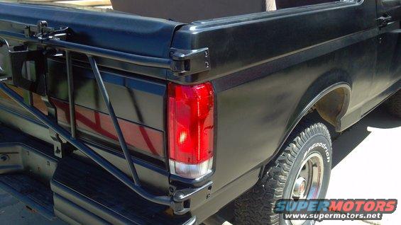 Rear view of a black 1987 Ford Bronco showing the taillight and tire. It has a metal rack attached to the back