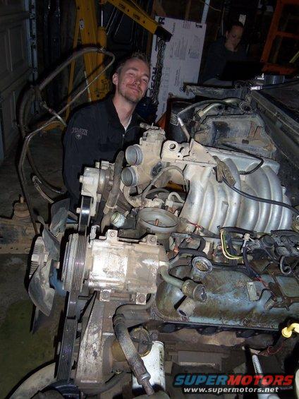 Engine assembly in a garage with a man smiling in the background