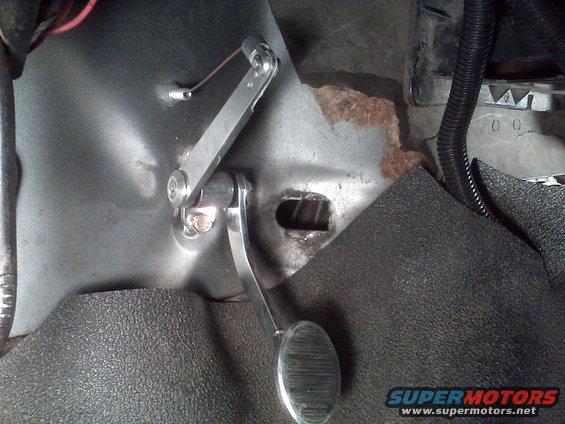 Close-up of a vehicle's accelerator pedal and linkage, with some rust visible on the floor pan
