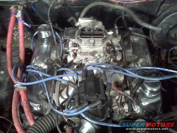 Close-up of engine bay with chrome valve covers, carburetor, and blue spark plug wires