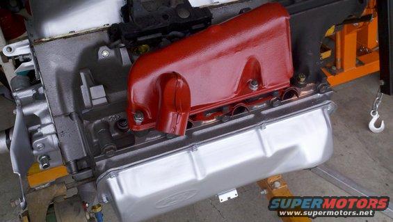 Engine block with red intake manifold and silver oil pan, supported by engine stands