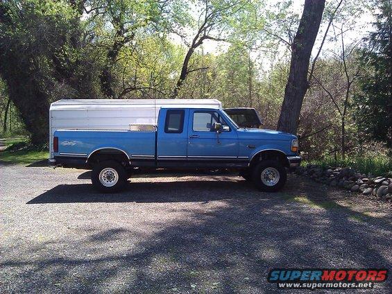 1992 Ford F-150 pickup truck, blue with white camper shell, parked on gravel