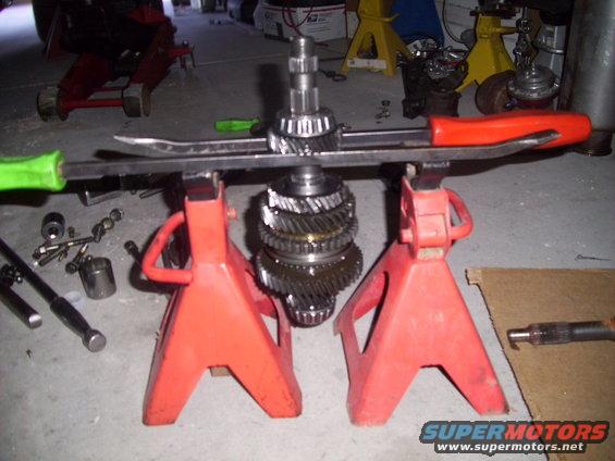 Transmission gears stacked on a shaft, held up by two red jack stands with tools nearby