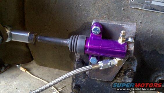 Purple hydraulic clutch slave cylinder mounted on metal bracket. Braided line attached