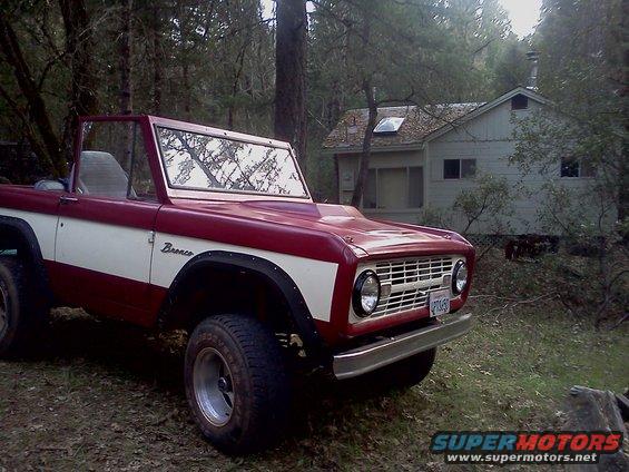 Red and white 1968 Ford Bronco parked in front of a cabin in the woods