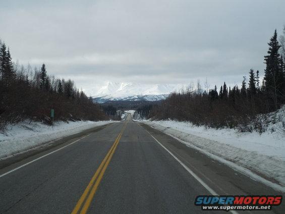 Snowy road leading to mountains under an overcast sky