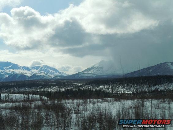 Snowy mountains and forest under a cloudy sky