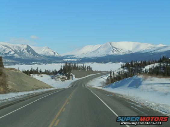 Winding asphalt road through a snowy mountain landscape under a clear blue sky