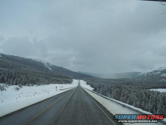 Highway through snowy forest and mountains under cloudy sky