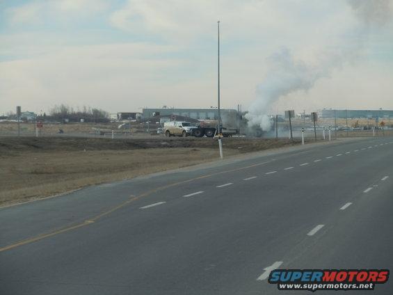 Side view of a truck emitting smoke on the side of a highway