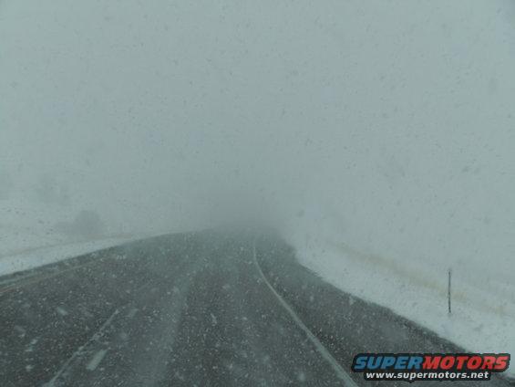 View from inside a vehicle driving on a snowy road with poor visibility