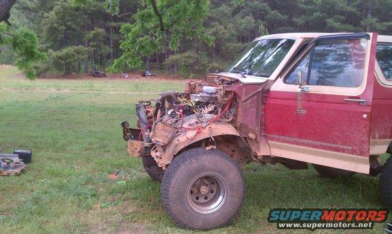 Red and tan Ford Bronco with hood removed, engine exposed, parked in a grassy area