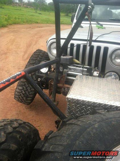Front of a Jeep Wrangler with a winch and a diamond plate toolbox, seen from behind another vehicle