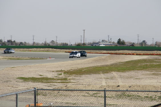 Cars on a racetrack with a silver convertible in the distance and two sedans closer
