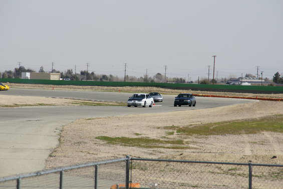 Three cars race on a track with a yellow car visible on the left