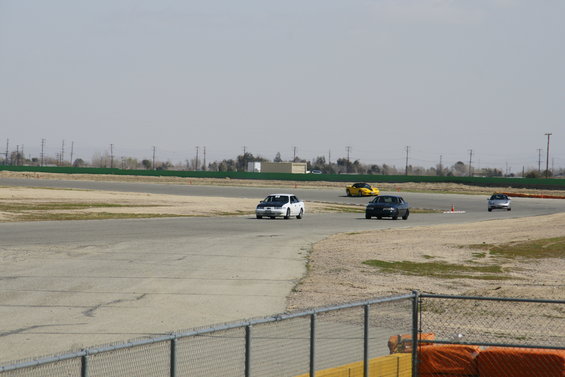 White car with black hood on race track, other cars visible
