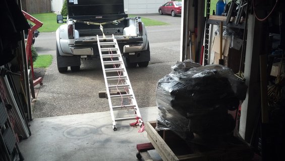 Pickup truck with its tailgate down and a ramp extending from the bed to the ground. A large, wrapped object is in the foreground