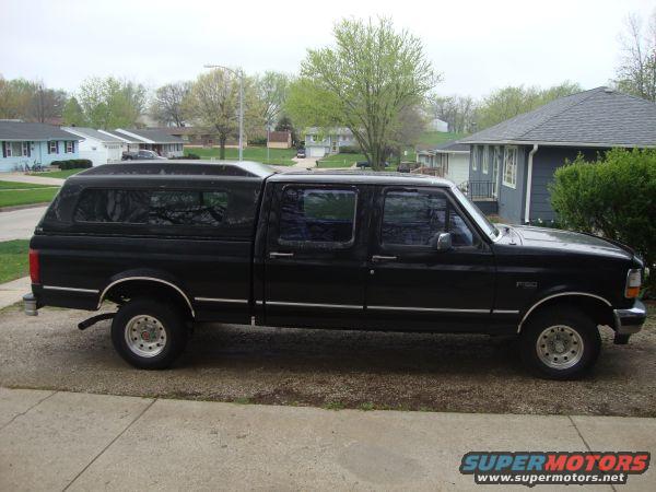 Black crew cab pickup truck with a camper shell parked on a driveway