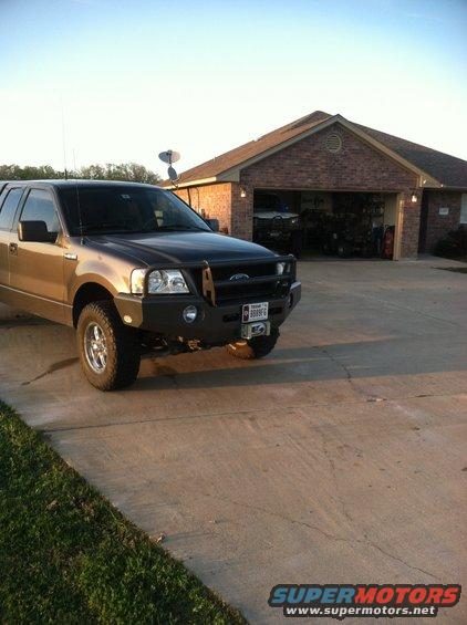 Gold Ford F-150 with aftermarket bumper parked in driveway in front of a brick house