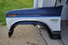 1986 Ford Bronco - A blue and white Ford Bronco fender, likely from a 1986 model, is shown removed from the vehicle.