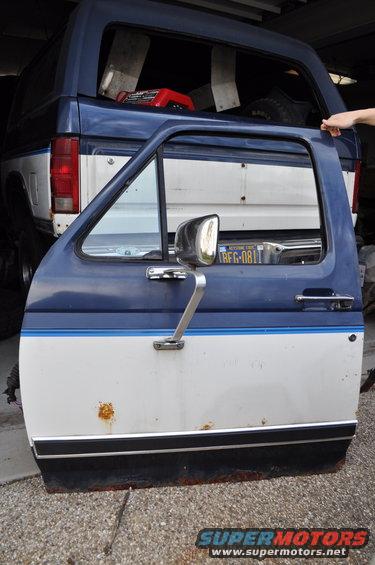1986 Ford Bronco door removed, showing rust. Another Bronco is visible behind it