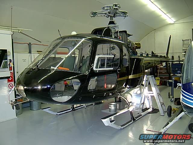 Black helicopter with gold stripe in hangar, another helicopter partially visible on the right