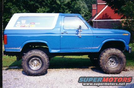 Blue Ford Bronco with a white top, lifted with large tires. Has some stickers on the rear window