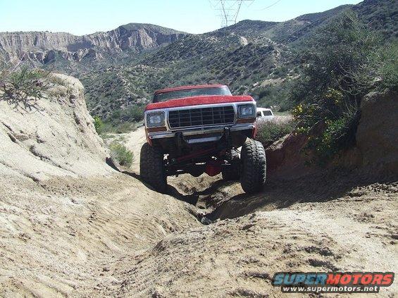 Red 1978 Ford Bronco off-roading on a dirt trail, front view