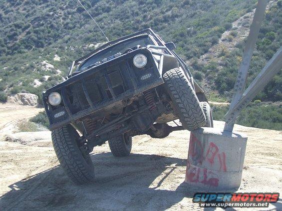 Off-road vehicle with roll cage on a dirt hill, one wheel on a concrete barrier