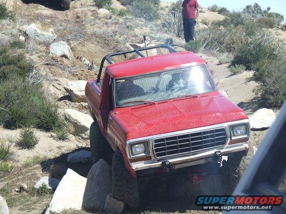 Red pickup truck with roll cage navigating rocky terrain