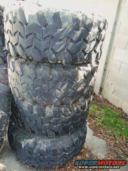 stack of four large, knobby off-road tires leaning against a cinder block wall