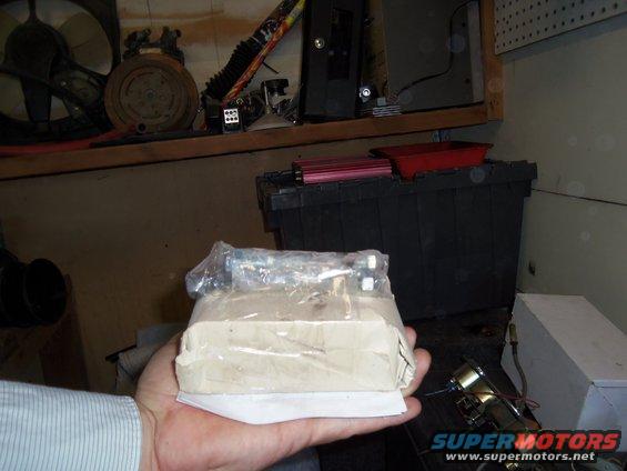 Part wrapped in plastic and paper held in a hand, with a Supermotors.net watermark