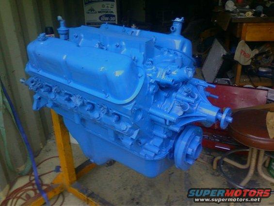 Blue painted V8 engine on an engine stand, with workshop clutter in background