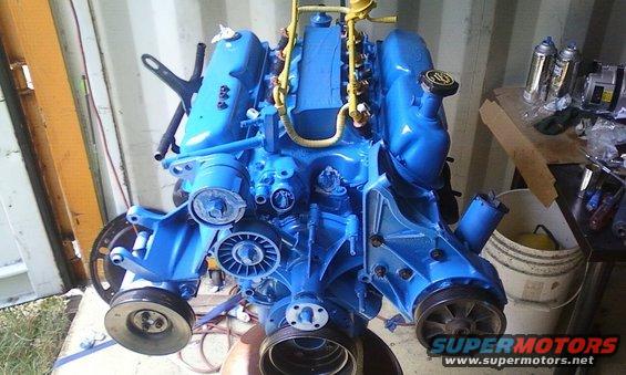 Blue engine assembly with yellow fuel lines and black hoses, viewed from the front